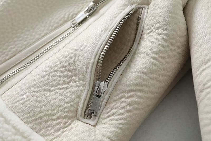 Close-up of a white aviator sheepskin jacket's zippered pocket, highlighting texture and premium craftsmanship.