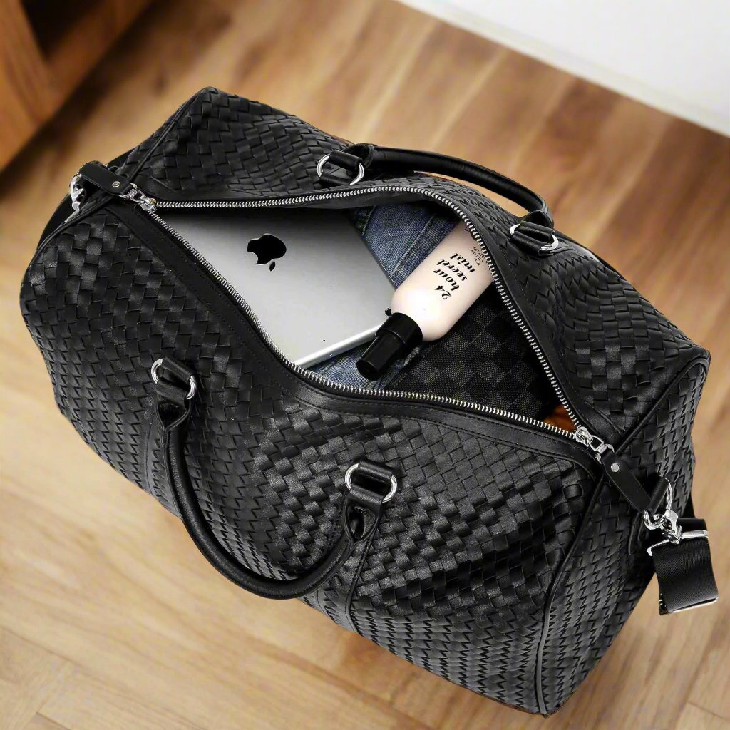 Black Kamau travel bag with woven texture, open to reveal organized compartments holding a laptop, denim, and a toiletries bottle.