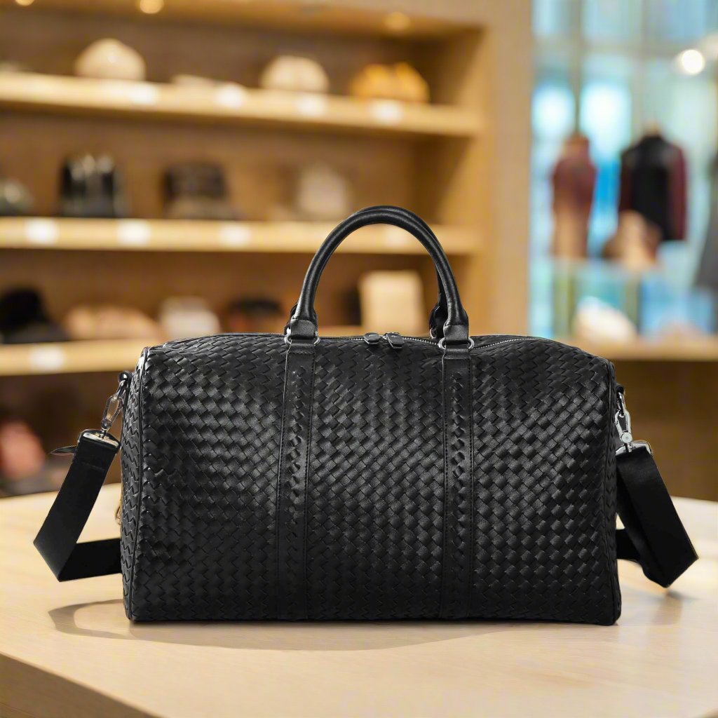 Black Kamau travel bag with elegant woven design on a table, showcasing spaciousness and stylish handles for easy carrying.