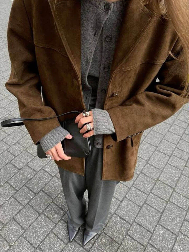 Stylish suede leather jacket with gray sweater and black clutch, showcasing a chic and elegant streetwear look.