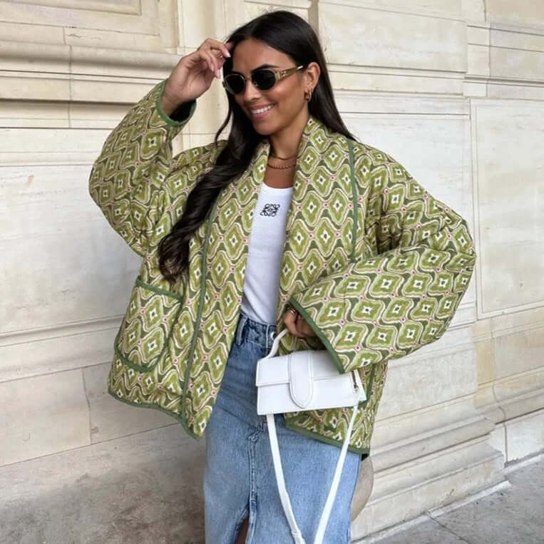 Woman wearing a stylish green patterned Swannie jacket with a white top and denim skirt, accessorized with sunglasses and a white purse.