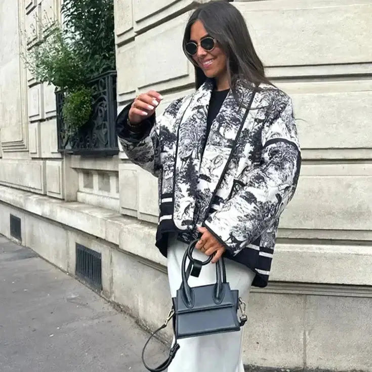 Woman in stylish Swannie jacket and sunglasses holding a chic black handbag on a city street.